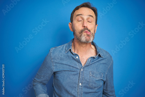 Handsome middle age senior man with grey hair over isolated blue background making fish face with lips, crazy and comical gesture. Funny expression.