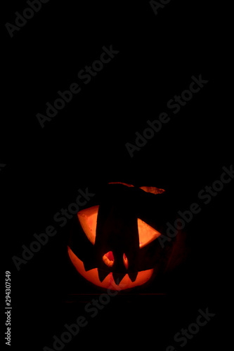 Scary face halloween pumpkin with glowing candle inside isolated on black background 