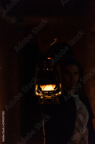 Portrait of man in hoodie holding out an old vintage kerosene lantern in his hand in the dark close up © godbamn