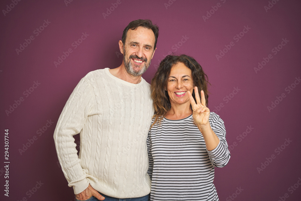 Naklejka premium Beautiful middle age couple wearing winter sweater over isolated purple background showing and pointing up with fingers number three while smiling confident and happy.