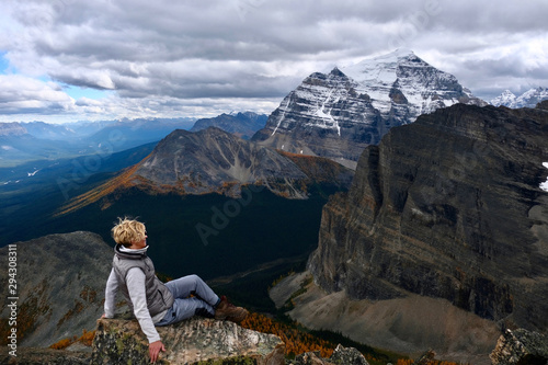 Successful woman hiker sitting on mountain top enjoying view of mountain valley with yellow larch trees from above. Lake Louise area. Banff National park. Alberta. Canada.