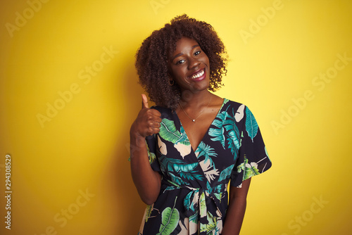 Young african afro woman wearing summer floral dress over isolated yellow background doing happy thumbs up gesture with hand. Approving expression looking at the camera with showing success.
