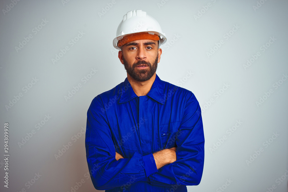 Handsome indian worker man wearing uniform and helmet over isolated white background skeptic and nervous, disapproving expression on face with crossed arms. Negative person. Handsome indian worker man wearing uniform and helmet over isolated white background skeptic and nervous, disapproving expression on face with crossed arms. Negative person.