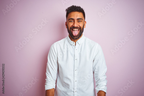 Young indian businessman wearing elegant shirt standing over isolated pink background sticking tongue out happy with funny expression. Emotion concept.