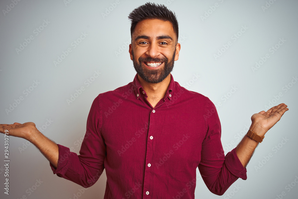 Young indian man wearing red elegant shirt standing over isolated grey background smiling showing both hands open palms, presenting and advertising comparison and balance Young indian man wearing red elegant shirt standing over isolated grey background smiling showing both hands open palms, presenting and advertising comparison and balance