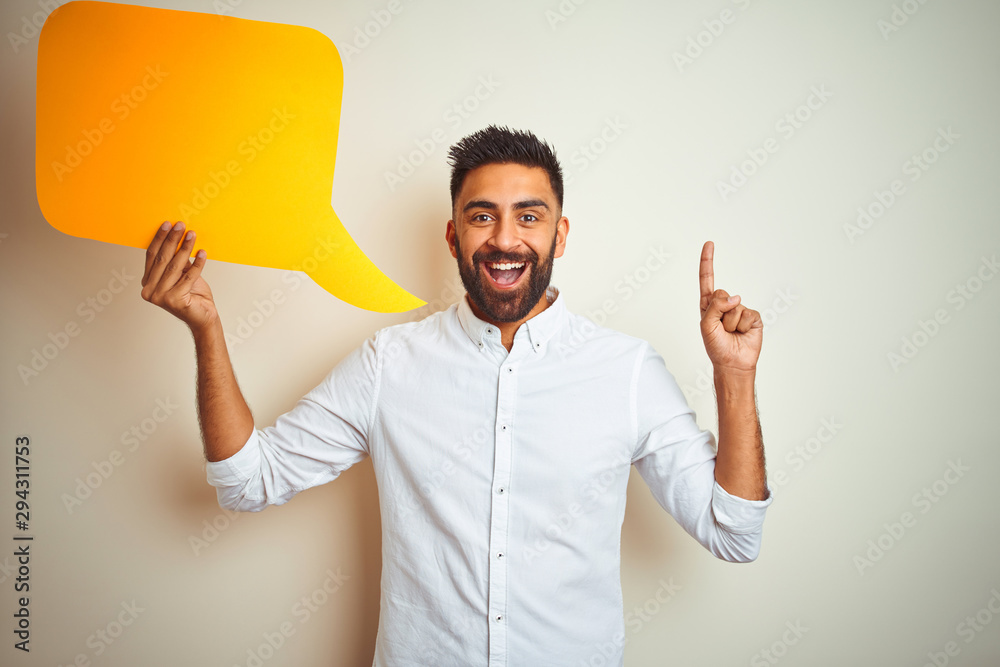 Young arab indian hispanic man holding speech bubble over isolated white background surprised with an idea or question pointing finger with happy face, number one