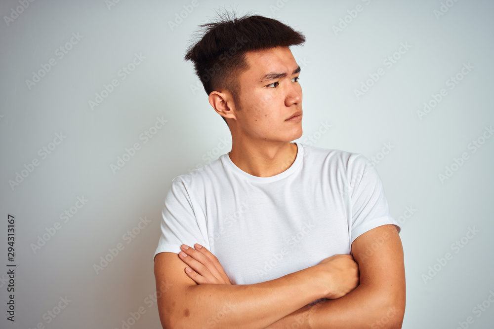 Young asian chinese man wearing t-shirt standing over isolated white background looking to the side with arms crossed convinced and confident Young asian chinese man wearing t-shirt standing over isolated white background looking to the side with arms crossed convinced and confident