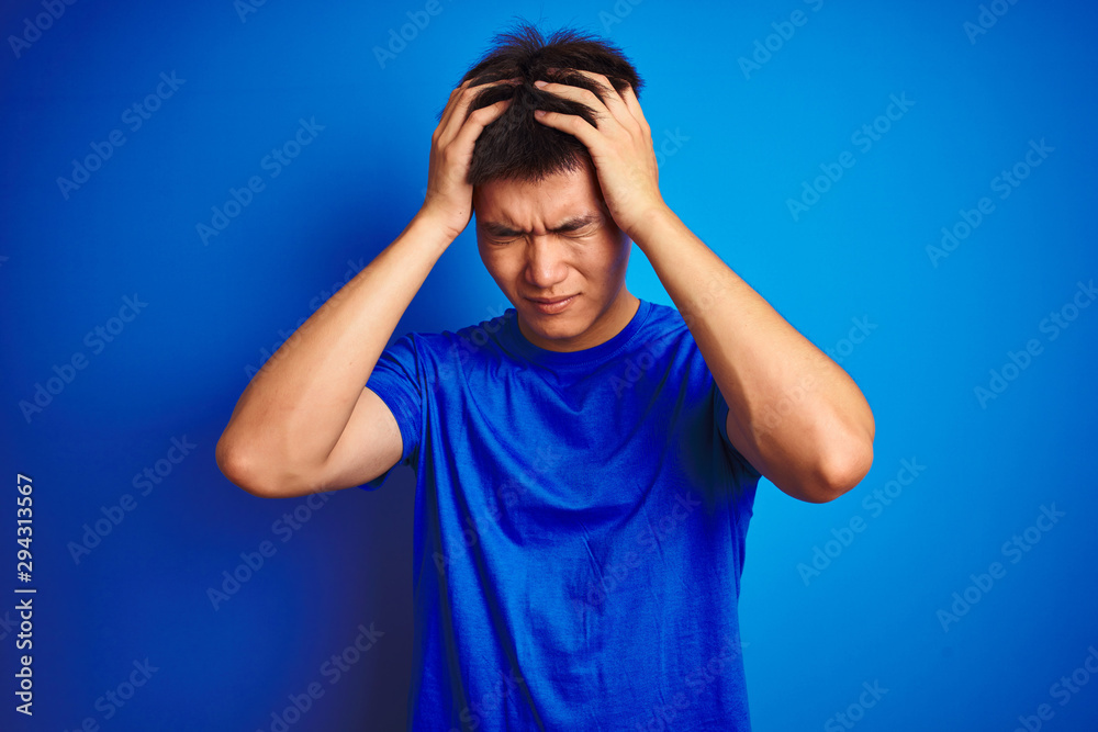 © Krakenimages.com - Young asian chinese man wearing t-shirt standing over isolated blue background suffering from headache desperate and stressed because pain and migraine. Hands on head. © Krakenimages.com - Young asian chinese man wearing t-shirt standing over isolated blue background suffering from headache desperate and stressed because pain and migraine. Hands on head.