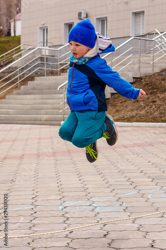 a five-year-old boy in a blue hat and jacket jumps over a rope high