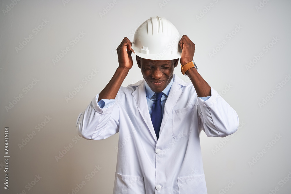 African american engineer man wearing coat and helmet over isolated white background suffering from headache desperate and stressed because pain and migraine. Hands on head. African american engineer man wearing coat and helmet over isolated white background suffering from headache desperate and stressed because pain and migraine. Hands on head.