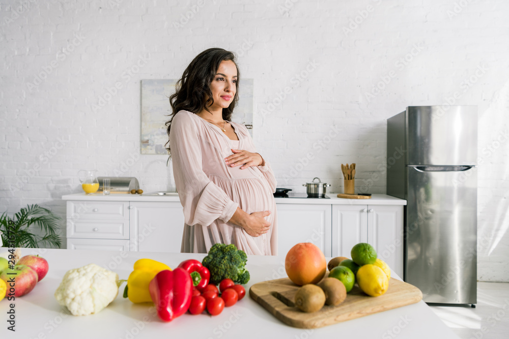 happy pregnant woman touching belly near tasty food on table