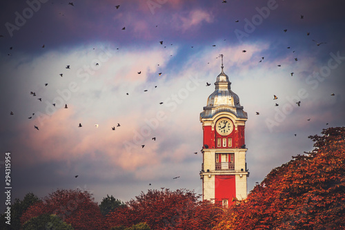 Old tower clock of railway station of Varna city, Bulgaria and flying birds at sunrise.image
