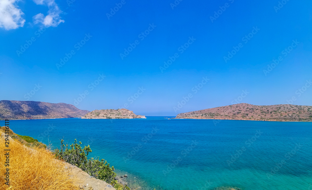 Spinalonga island with blue sky and transparent sea. Elounda, Spinalonga, Crete, Greece. Traveling at Crete, summer vacations and destinations. Copy space for text. Panoramic view HD.