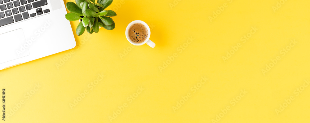 Fototapeta Office desktop with laptop, coffee and small succulent on yellow background with copyspace. Panoramic banner