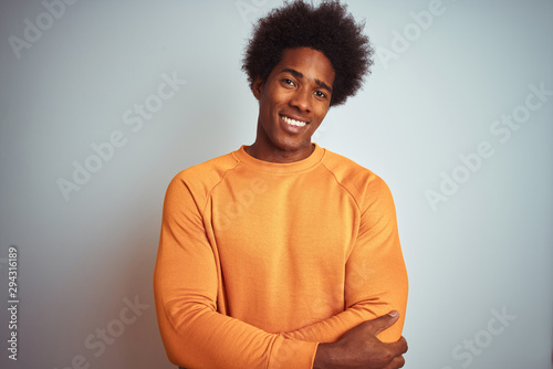 Young american man with afro hair wearing orange sweater over isolated white background happy face smiling with crossed arms looking at the camera. Positive person.