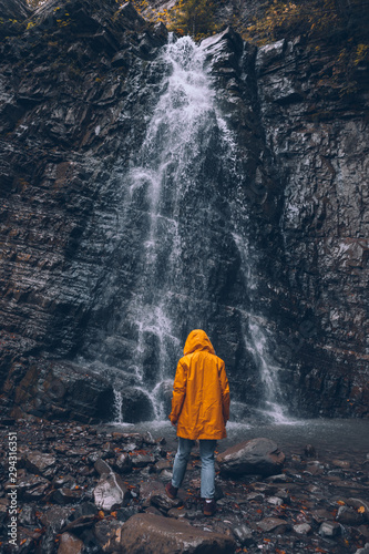 woman in yellow raincoat at autumn waterfall