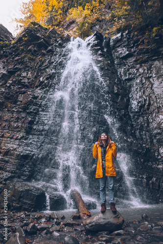 woman in yellow raincoat at autumn waterfall