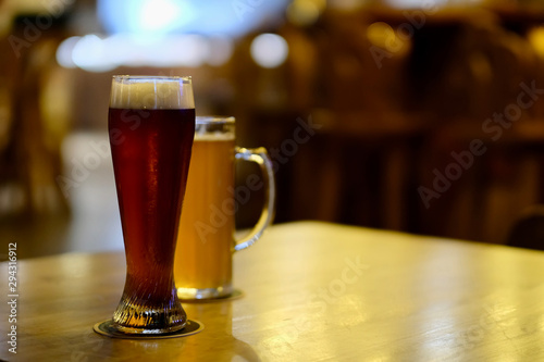 close up wheat beer glass and beer mug with beer on wooden shiny table in bar. Blur background