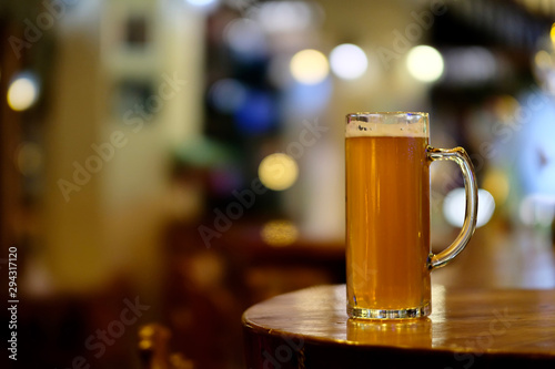 close up one mug of beer on wooden shiny bar counter. Blur colorful background