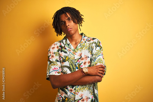 Afro man with dreadlocks on vacation wearing summer shirt over isolated yellow background skeptic and nervous  disapproving expression on face with crossed arms. Negative person.