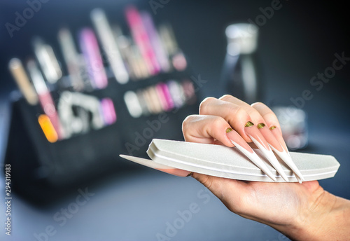 Long nails manicure. Woman hand with file. Beautiful nails art design with brusches background. photo