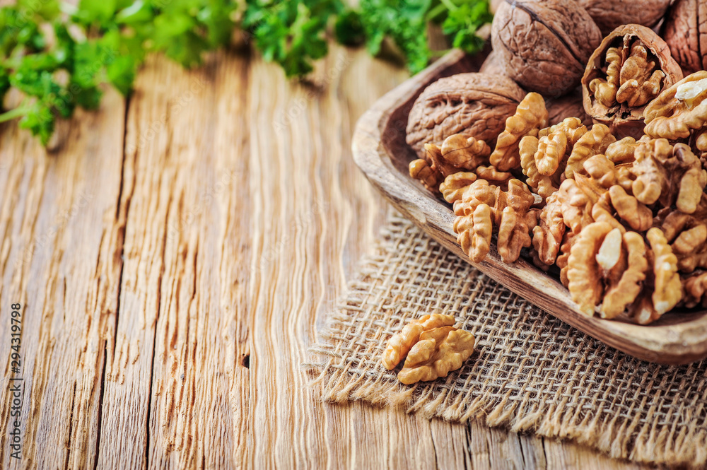 Whole walnuts in wooden bowl. Walnuts concept with green leaves on jute fabric. Whole walnuts in wooden bowl. Walnuts concept with green leaves on jute fabric.