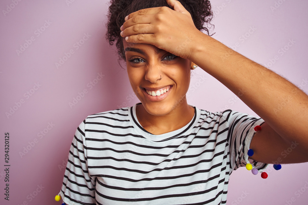 African american woman wearing navy striped t-shirt standing over isolated pink background stressed with hand on head, shocked with shame and surprise face, angry and frustrated. Fear