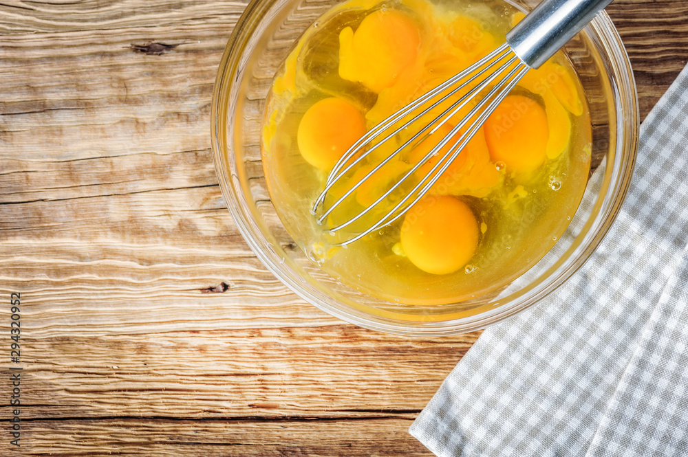 Whipped eggs. Woman whisking fresh eggs in glass bowl on wooden table. Whipped eggs. Woman whisking fresh eggs in glass bowl on wooden table.