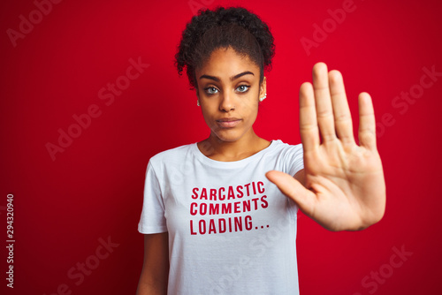 Afro american woman wearing funny t-shirt with irony comments over isolated red background with open hand doing stop sign with serious and confident expression, defense gesture