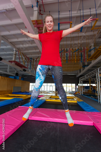 Fitness, fun, leisure and sport activity concept - Young happy woman jumping on a trampoline indoors