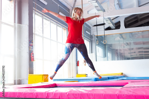 Fitness  fun  leisure and sport activity concept - Young happy woman jumping on a trampoline indoors