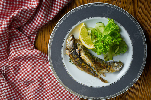 Close up Grilled fish sprat with salad on white plate in composition with red cloth on wooden table. Food photo background. Seafood