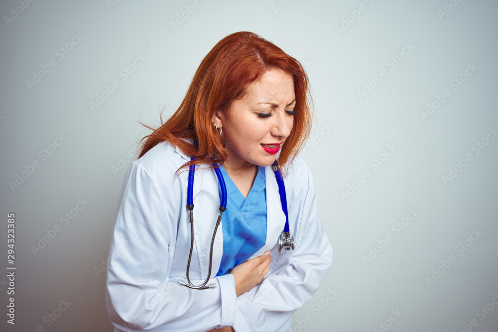 Young redhead doctor woman using stethoscope over white isolated background with hand on stomach because indigestion, painful illness feeling unwell. Ache concept.