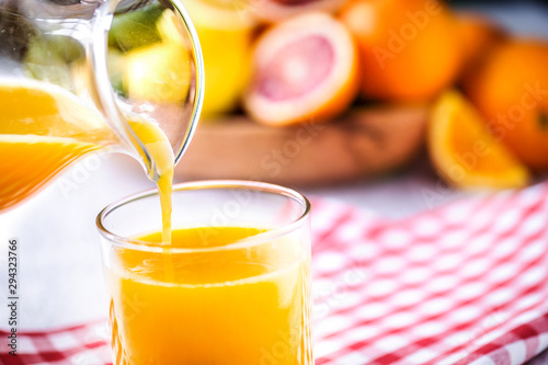 Pouring orange juice in to glass. Tropical fruits juice in glass with orange, lime and grep. Fresh orange nectar. photo