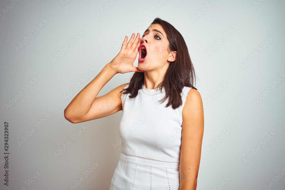 Young beautiful woman wearing dress standing over white isolated background shouting and screaming loud to side with hand on mouth. Communication concept. Young beautiful woman wearing dress standing over white isolated background shouting and screaming loud to side with hand on mouth. Communication concept.