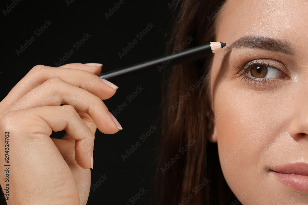 Obraz premium Beautiful young woman with pencil for eyebrows on dark background, closeup