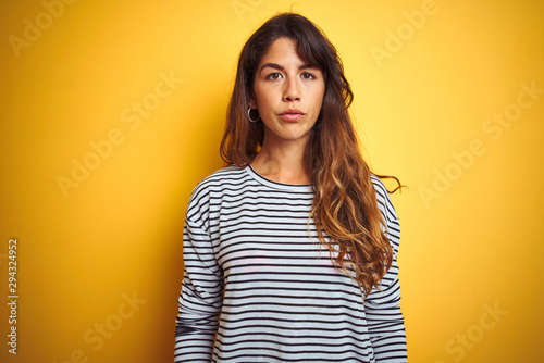 Young beautiful woman wearing stripes t-shirt standing over yelllow isolated background Relaxed with serious expression on face. Simple and natural looking at the camera. photo