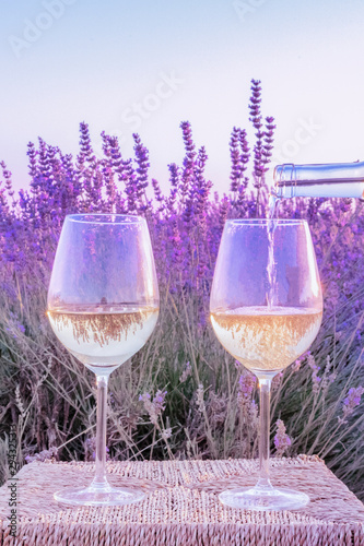 Lavender wine. White wine poured from a bottle into glasses against a lavender field background, toned image