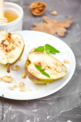 Tasty roast pears with honey and walnuts on white plates on grey background table.