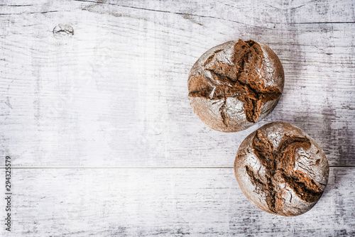 Dark baked buns on wooden white table. Top view of small rolls of tasty bread.