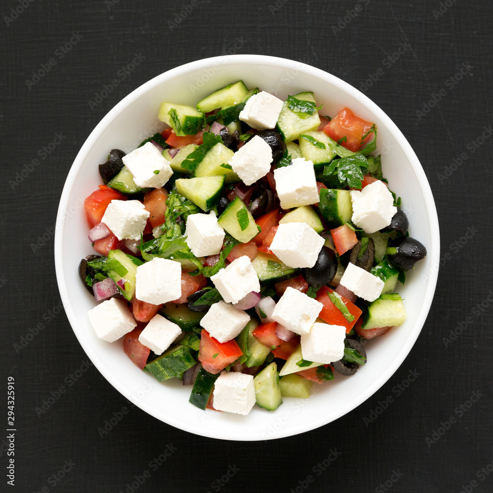 Homemade Shepherd's salad with cucumbers, feta and parsley in a white bowl on a black background, top view. From above, overhead, flat lay. Close-up.