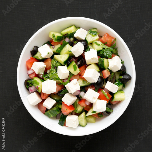 Homemade Shepherd's salad with cucumbers, feta and parsley in a white bowl on a black background, top view. From above, overhead, flat lay. Close-up.