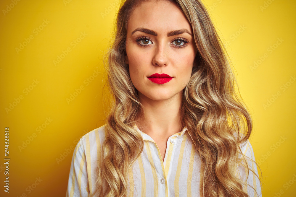 Young beautiful woman wearing stripes shirt standing over yellow isolated background with a confident expression on smart face thinking serious Young beautiful woman wearing stripes shirt standing over yellow isolated background with a confident expression on smart face thinking serious