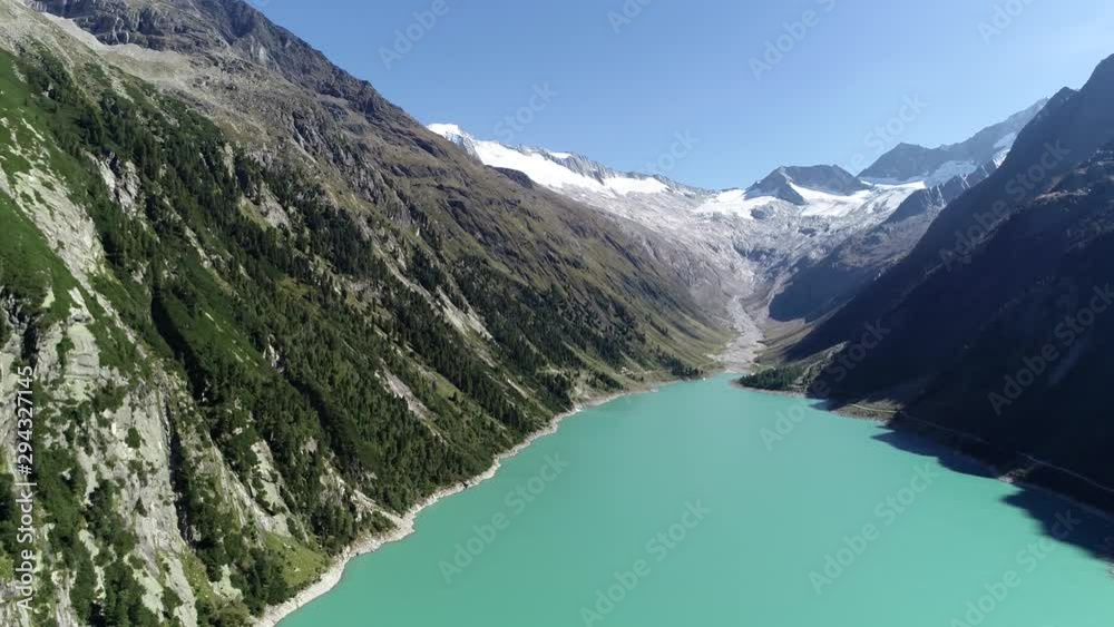 Aerial view from above turquoise colored lake panning from alps glacier left past mountain range to modern dam proving sustainable renewable enegery from water pressure 4k high resolution footage