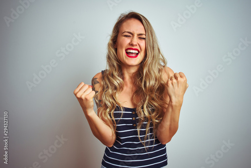 Young beautiful woman wearing stripes t-shirt standing over white isolated background very happy and excited doing winner gesture with arms raised, smiling and screaming for success