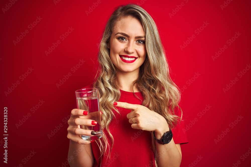 Young beautiful woman drinking a glass of water over red isolated background very happy pointing with hand and finger Young beautiful woman drinking a glass of water over red isolated background very happy pointing with hand and finger