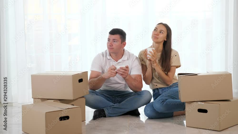 husband and wife sit on white floor among cardboard boxes and enjoy hot coffee at new beautiful home with light interior husband and wife sit on white floor among cardboard boxes and enjoy hot coffee at new beautiful home with light interior