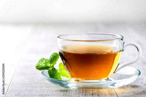 Green hot tea in clear glass cup on white table. Fresh tea with mint leaf.