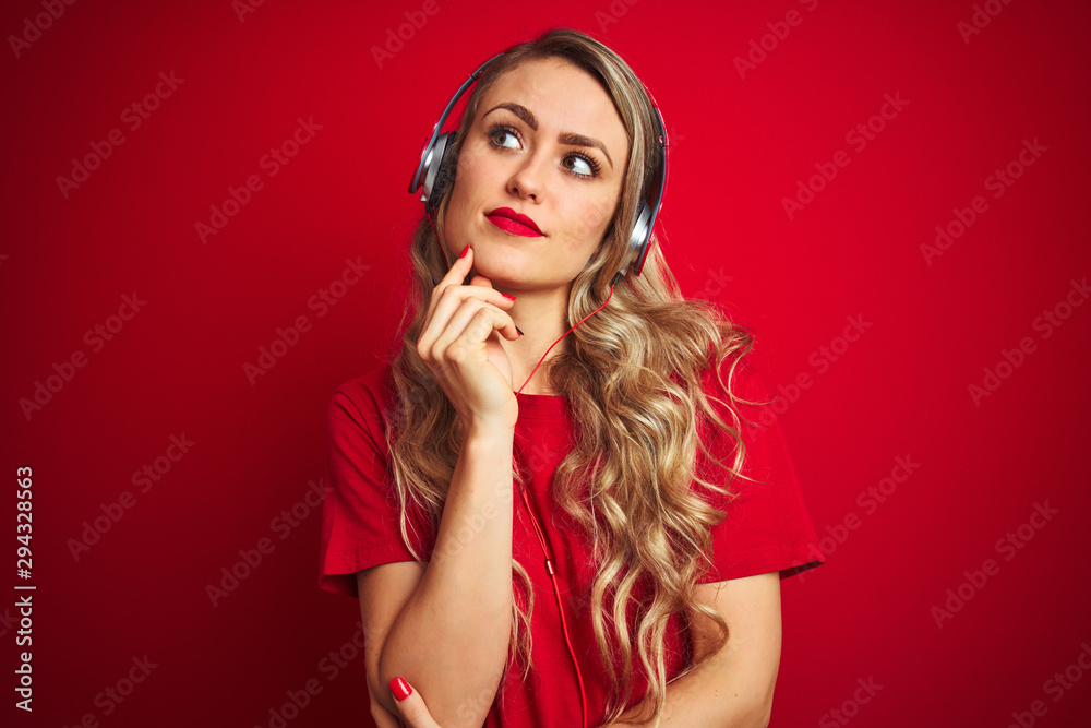 Young beautiful woman wearing headphones over red isolated background with hand on chin thinking about question, pensive expression. Smiling with thoughtful face. Doubt concept.