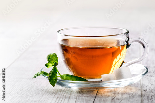 Hot cup of tea on white rustic table. Tea in clear glass on white with sugar and mint leaf.
